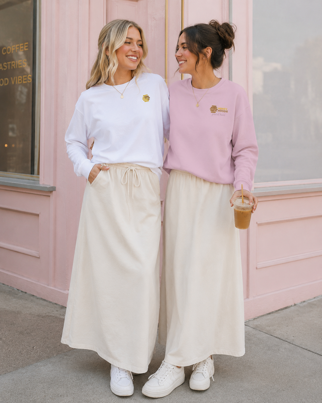 Two women wearing matching sweatshirts and skirts standing in front of a pink building.